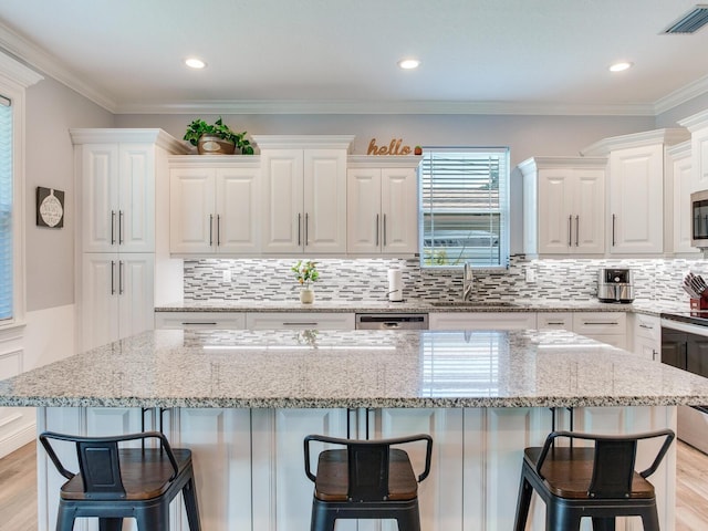 kitchen with sink, a kitchen breakfast bar, a center island, light stone counters, and white cabinets