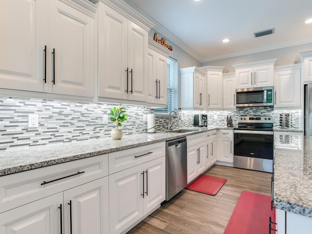 kitchen featuring sink, white cabinetry, crown molding, light hardwood / wood-style flooring, and appliances with stainless steel finishes