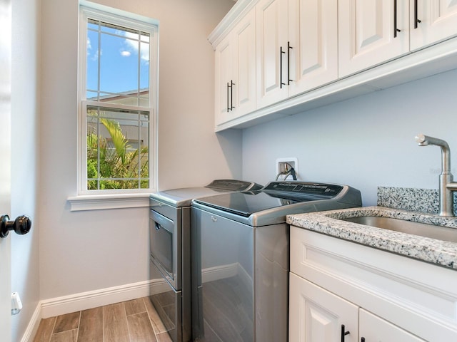 clothes washing area featuring cabinets, wood-type flooring, washer and clothes dryer, and sink