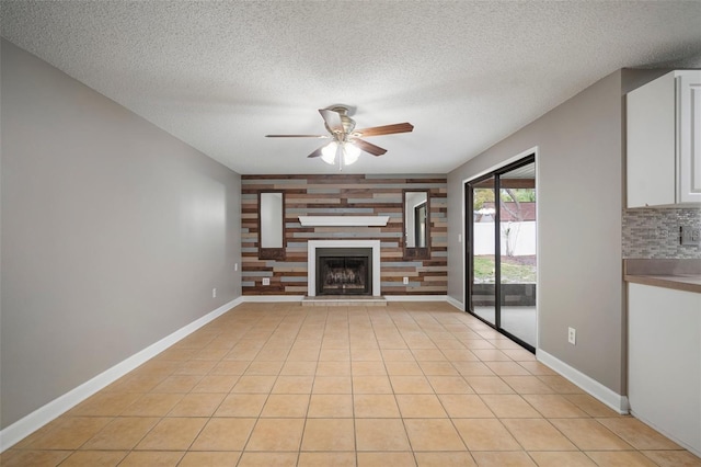 unfurnished living room with light tile patterned floors, a textured ceiling, a large fireplace, and ceiling fan