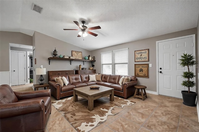 tiled living room with ceiling fan, vaulted ceiling, and a textured ceiling