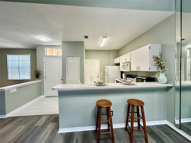 2116 Nantucket Dr Unit 19, Sun City Center, FL 33573 - kitchen with white cabinets, a peninsula, wood finished floors, white appliances, and light countertops