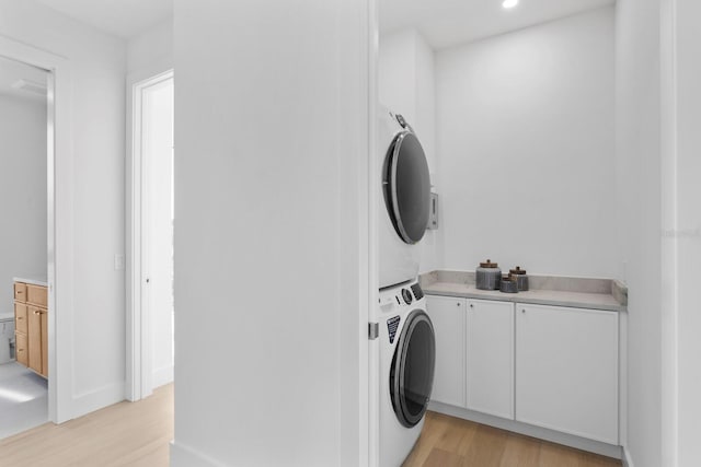 laundry room with light wood-type flooring, cabinets, and stacked washer / drying machine