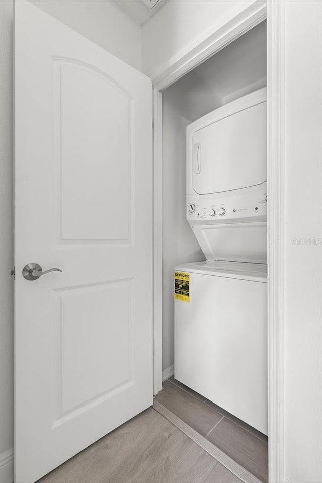 washroom with hardwood / wood-style flooring and stacked washer and clothes dryer