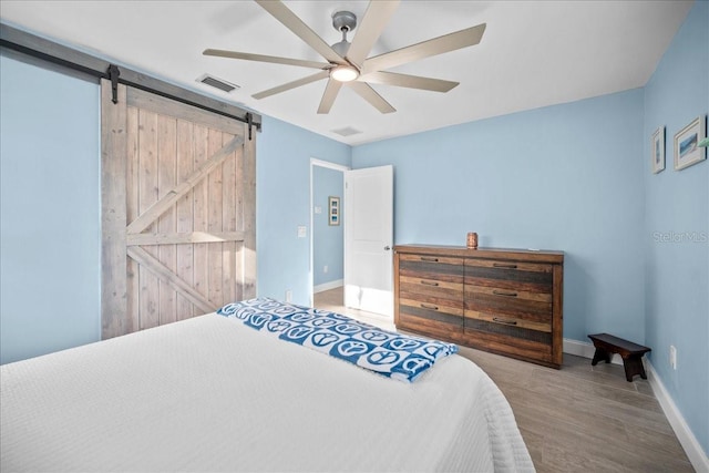 bedroom featuring hardwood / wood-style flooring, a barn door, and ceiling fan