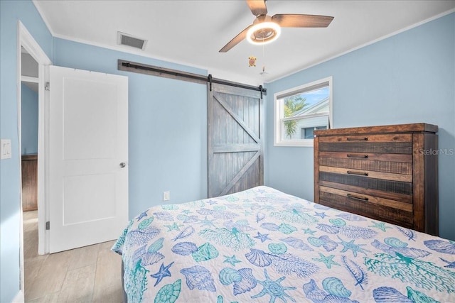 bedroom with crown molding, light hardwood / wood-style flooring, a barn door, and ceiling fan