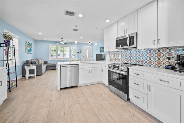 kitchen with sink, kitchen peninsula, white cabinets, stainless steel appliances, and backsplash