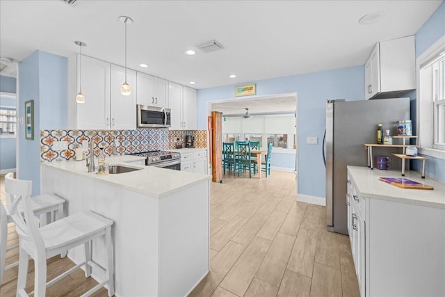 kitchen with a sink, light countertops, appliances with stainless steel finishes, wood tiled floor, and tasteful backsplash