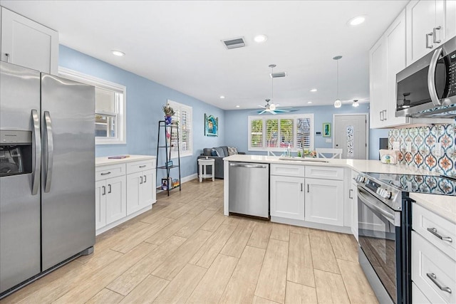 kitchen featuring stainless steel appliances, a peninsula, visible vents, open floor plan, and light countertops