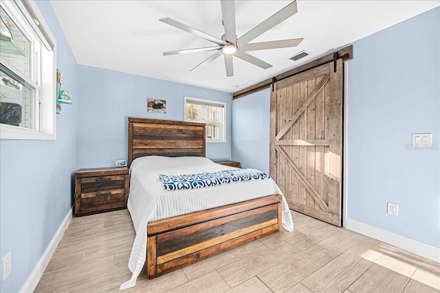 bedroom with light wood-style floors, a barn door, visible vents, and baseboards