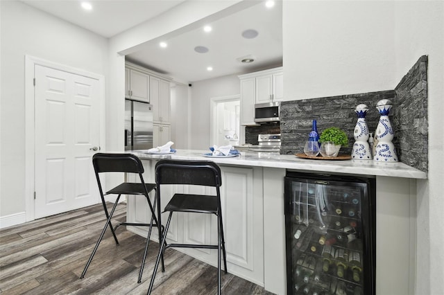 kitchen featuring wine cooler, appliances with stainless steel finishes, a kitchen bar, and hardwood / wood-style floors