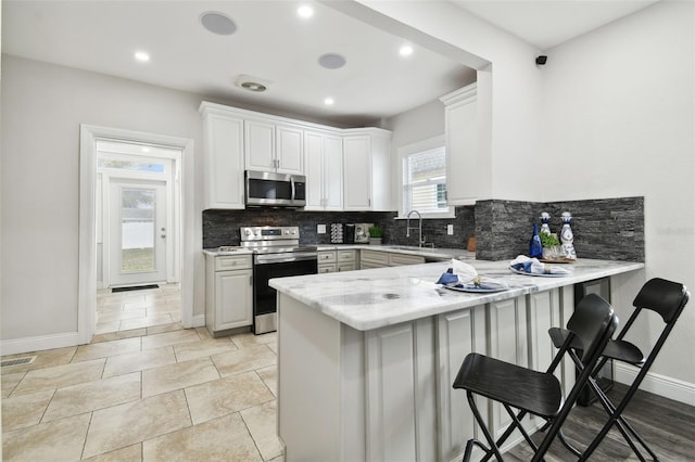 kitchen with white cabinetry, sink, a kitchen breakfast bar, kitchen peninsula, and stainless steel appliances