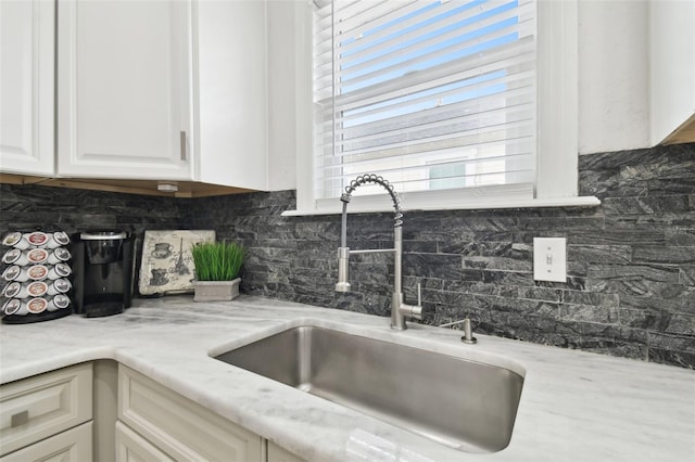 kitchen featuring light stone counters, white cabinets, sink, and backsplash