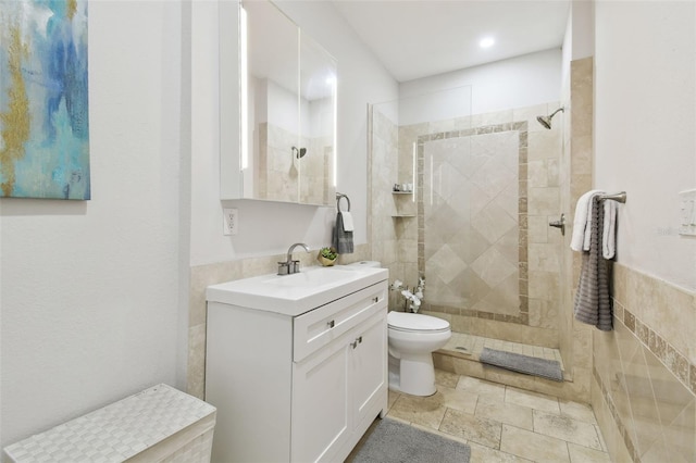 bathroom featuring tiled shower, vanity, toilet, and tile walls