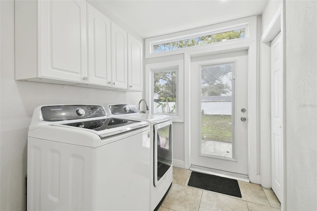 clothes washing area with separate washer and dryer, light tile patterned floors, a wealth of natural light, and cabinets