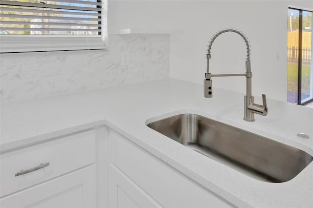 room details with light stone countertops, sink, decorative backsplash, and white cabinets