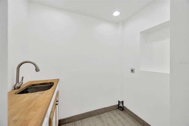 washroom with sink, hookup for an electric dryer, cabinets, and light wood-type flooring