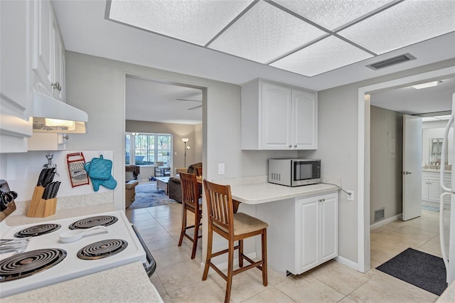 kitchen with a kitchen bar, white cabinetry, light tile patterned floors, range with electric cooktop, and ceiling fan