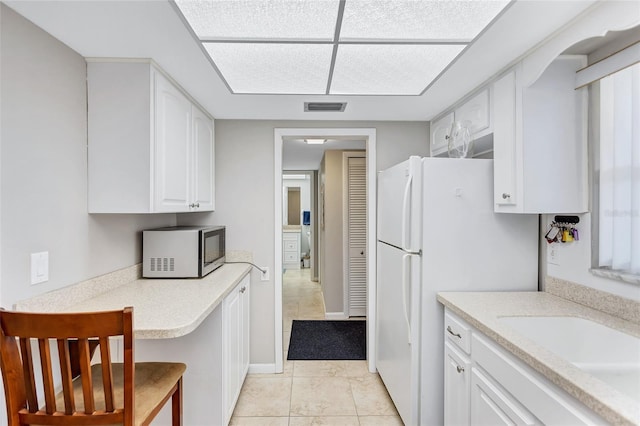 kitchen featuring light tile patterned flooring, sink, a breakfast bar area, white cabinetry, and white fridge