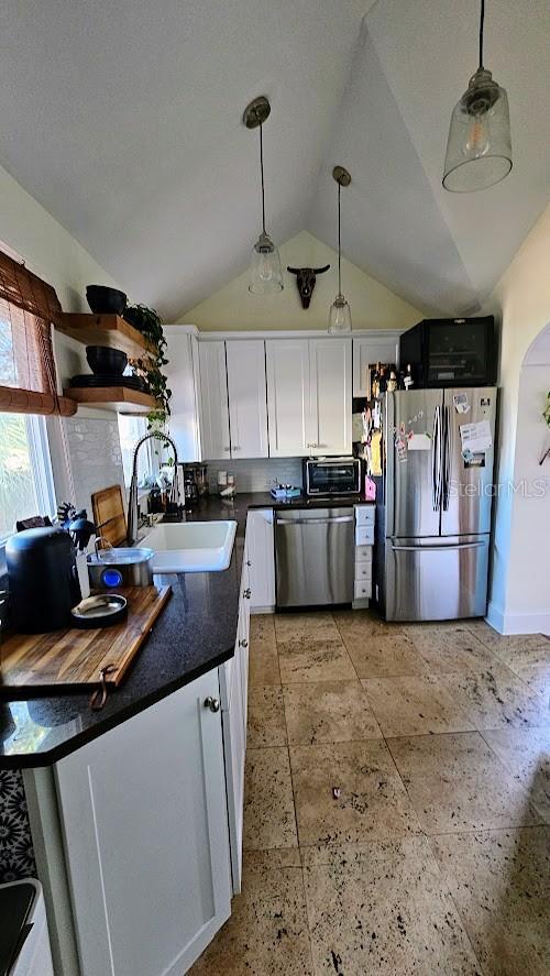 kitchen featuring appliances with stainless steel finishes, decorative light fixtures, lofted ceiling, sink, and white cabinets