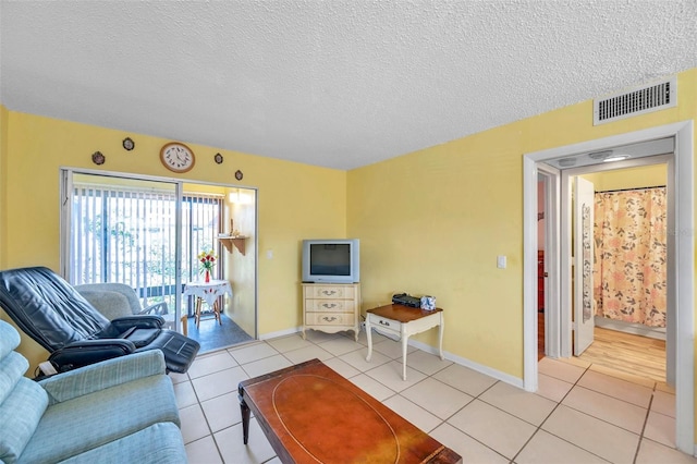 living area featuring light tile patterned floors, a textured ceiling, visible vents, and baseboards