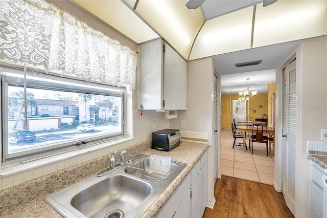 kitchen with visible vents, backsplash, a sink, light countertops, and a notable chandelier