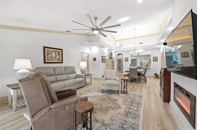 living room with crown molding, ceiling fan with notable chandelier, light hardwood / wood-style floors, and a tray ceiling