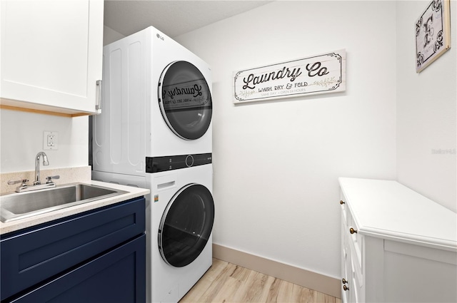 washroom featuring cabinets, stacked washer and clothes dryer, sink, and light wood-type flooring