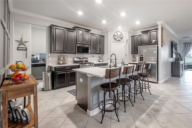 kitchen with appliances with stainless steel finishes, a kitchen bar, light tile patterned floors, crown molding, and a center island with sink