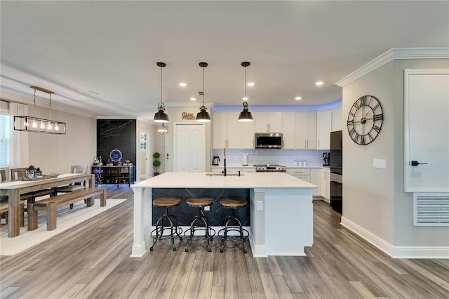 kitchen featuring hanging light fixtures, white cabinetry, appliances with stainless steel finishes, and an island with sink