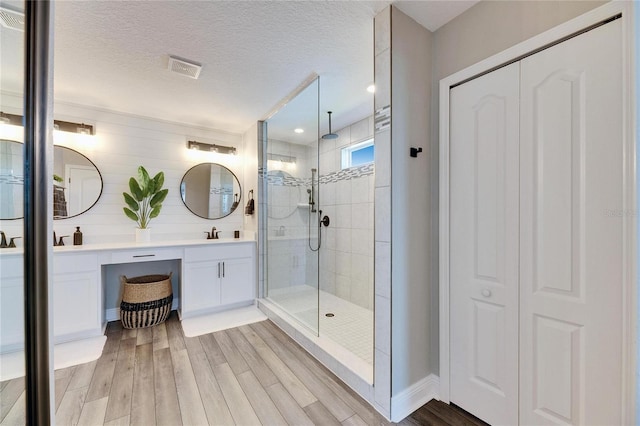 bathroom featuring vanity, hardwood / wood-style floors, a textured ceiling, and a tile shower