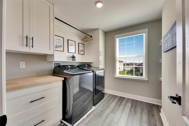 clothes washing area featuring cabinets, washer and clothes dryer, light hardwood / wood-style floors, and a textured ceiling