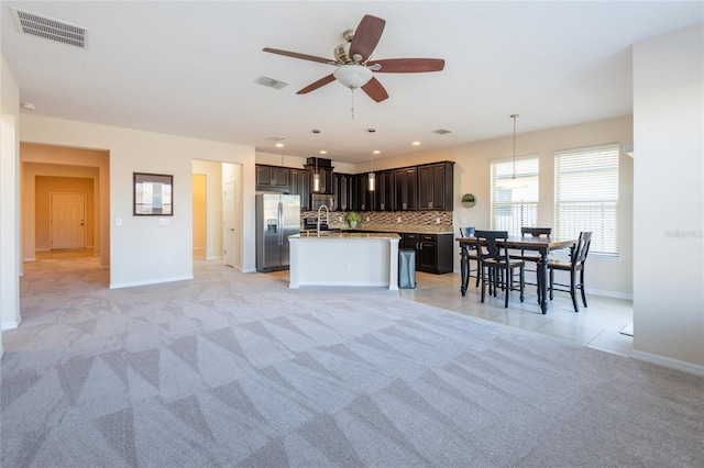 kitchen with pendant lighting, stainless steel fridge, decorative backsplash, dark brown cabinets, and a center island with sink