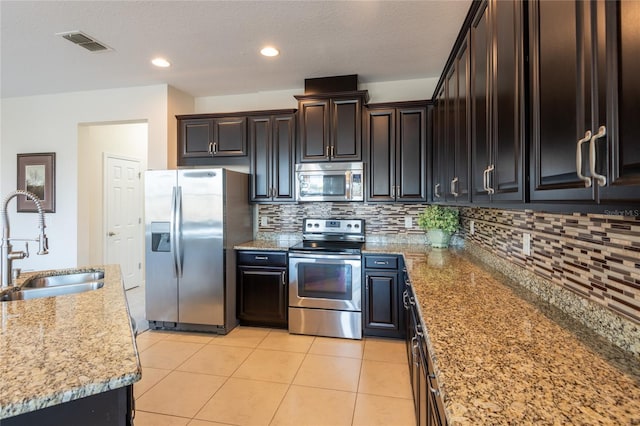 kitchen featuring dark brown cabinetry, sink, light tile patterned floors, appliances with stainless steel finishes, and light stone countertops