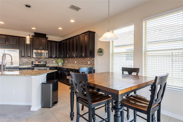 kitchen with appliances with stainless steel finishes, backsplash, hanging light fixtures, light stone countertops, and dark brown cabinets