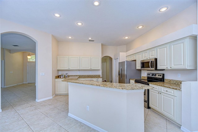 kitchen featuring light stone counters, stainless steel appliances, a center island with sink, and white cabinets