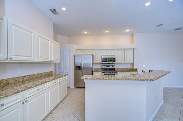 kitchen with light tile patterned floors, appliances with stainless steel finishes, light stone counters, white cabinets, and a kitchen island