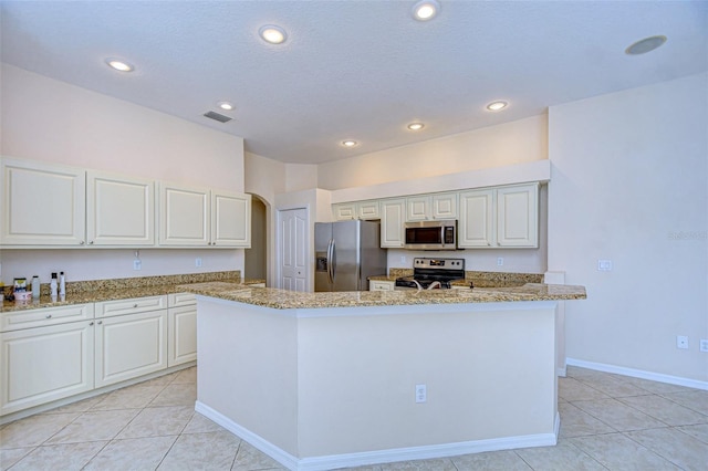 kitchen with white cabinetry, stainless steel appliances, a center island, light stone counters, and light tile patterned flooring