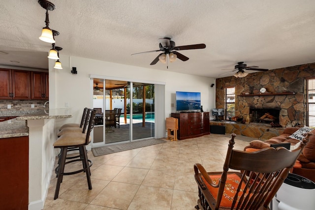 living room with ceiling fan, light tile patterned floors, a fireplace, and a textured ceiling