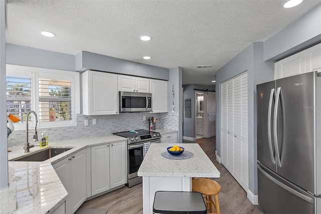 kitchen with sink, appliances with stainless steel finishes, a center island, white cabinets, and a barn door