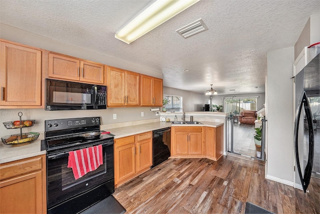 kitchen featuring sink, dark wood-type flooring, black appliances, a textured ceiling, and kitchen peninsula