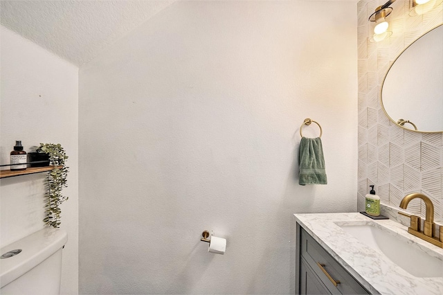 bathroom with vanity, vaulted ceiling, a textured ceiling, and toilet