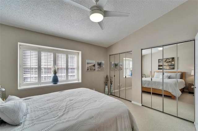 carpeted bedroom with multiple closets, vaulted ceiling, ceiling fan, and a textured ceiling