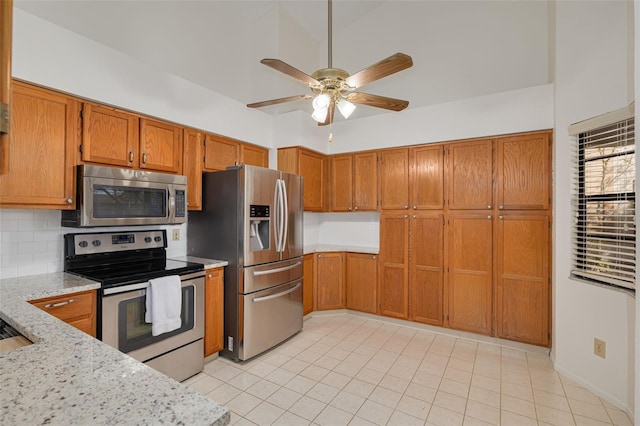 kitchen featuring tasteful backsplash, light tile patterned floors, ceiling fan, stainless steel appliances, and light stone countertops