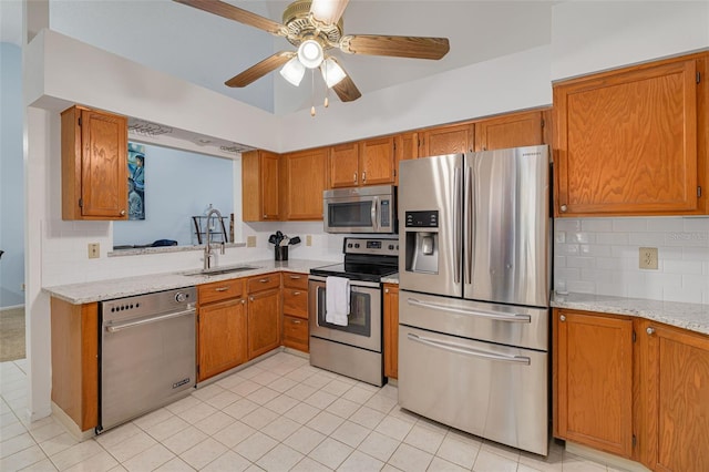 kitchen with sink, backsplash, ceiling fan, stainless steel appliances, and light stone countertops