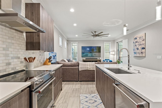 kitchen featuring wall chimney exhaust hood, modern cabinets, appliances with stainless steel finishes, light countertops, and a sink