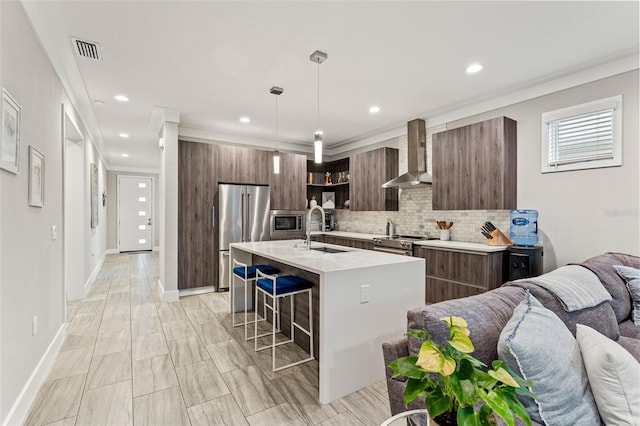 kitchen featuring modern cabinets, appliances with stainless steel finishes, open floor plan, wall chimney range hood, and a sink