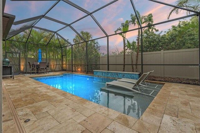 pool at dusk featuring a lanai, a patio area, a fenced backyard, and a fenced in pool