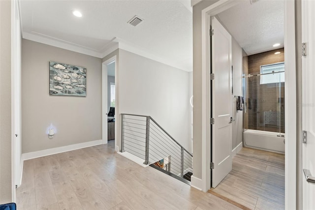 hallway featuring visible vents, a textured ceiling, an upstairs landing, light wood-type flooring, and baseboards