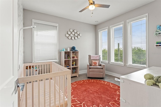 bedroom featuring a nursery area, a ceiling fan, baseboards, and wood finished floors